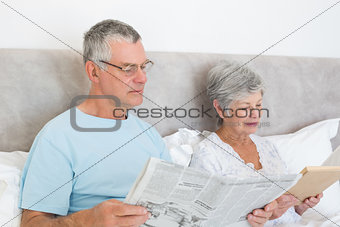 Senior couple with newspaper and book in house
