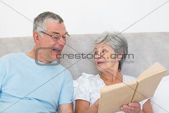 Senior woman showing book to husband in bed