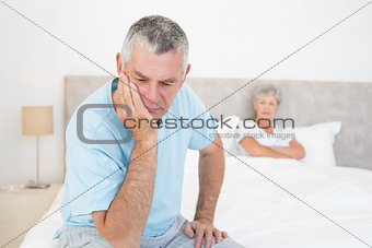 Disappointed senior man with woman in background