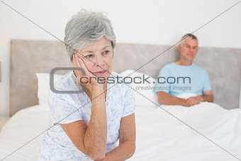 Sad senior woman on bed with husband in background