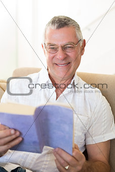 Senior man holding book on sofa