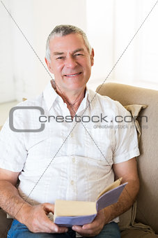 Smiling senior man holding book on sofa