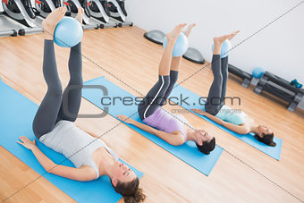 Sporty women holding balls between ankles in fitness studio
