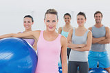 Instructor holding exercise ball with fitness class in background