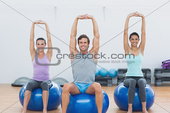 Sporty people stretching up hands on exercise balls at gym