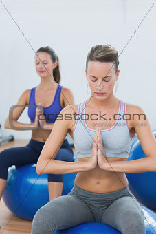 Women with joined hands and eyes closed on exercise balls