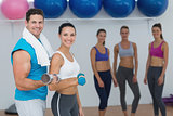 Couple holding dumbbells with fitness class in background