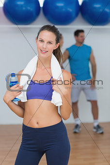 Portrait of a fit female holding water bottle with a man in background at gym