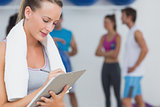 Trainer writing on clipboard with fitness class in background at gym