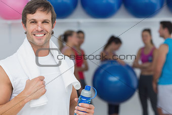Man holding water bottle with friends in background at fitness studio