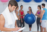 Trainer writing in clipboard with fitness class in background