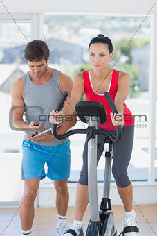 Fit woman with male instructor working out at spinning class
