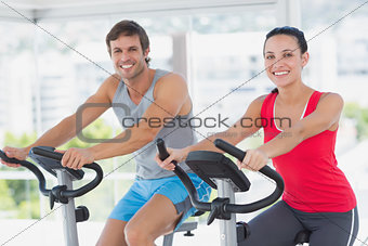 Smiling young couple working out at spinning class