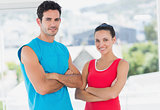 Fit couple with arms crossed in bright exercise room