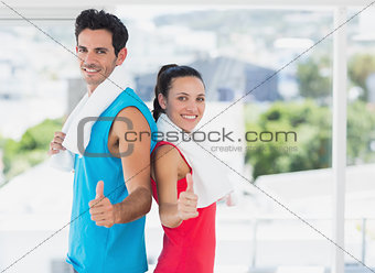 Fit couple gesturing thumbs up in bright exercise room