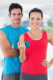 Fit couple standing with dumbbell in bright exercise room