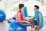 Instructor and woman with exercise ball at a bright gym