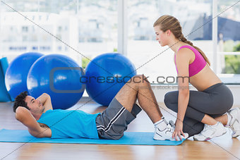 Female trainer helping man with his exercises at gym
