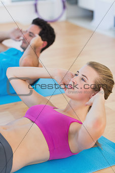 Determined young couple doing sit ups at gym