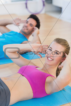 Smiling young couple doing sit ups at gym
