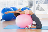 Side view of a fit woman exercising on fitness ball at gym