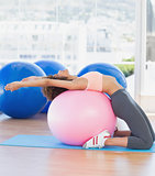 Side view of a fit woman exercising on fitness ball at gym