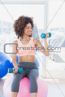 Woman exercising with dumbbells on fitness ball in gym