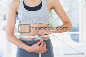 Mid section of a woman measuring waist in fitness studio