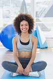 Fit woman sitting on exercise mat in fitness studio