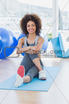 Fit woman sitting on exercise mat in fitness studio