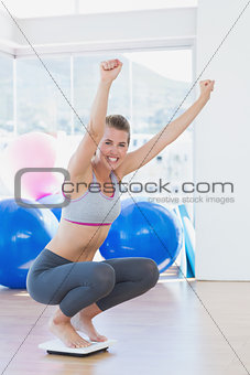 Fit woman cheering on scale in exercise room