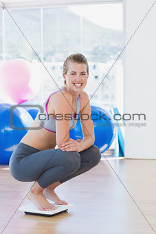 Fit young woman crouching on scale in exercise room