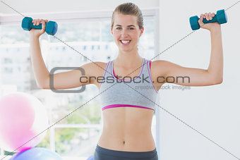 Smiling woman exercising with dumbbells in fitness studio
