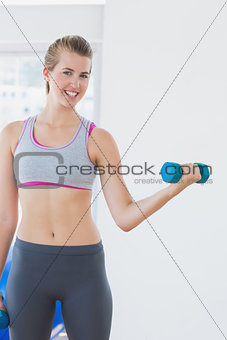 Young woman exercising with dumbbell in fitness studio