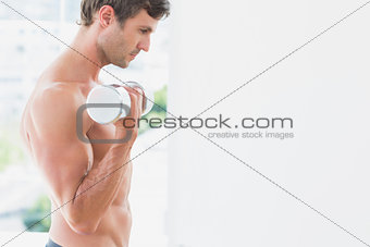 Serious young man exercising with dumbbell in fitness studio