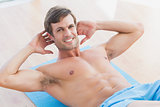 Smiling shirtless young man doing sit ups in fitness studio