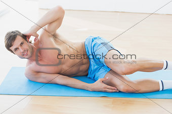 Smiling shirtless young man exercising in fitness studio