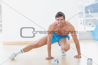 Sporty shirtless young man exercising in fitness studio