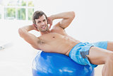 Shirtless man exercising on fitness ball in gym