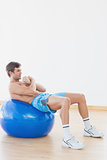 Shirtless man exercising on fitness ball in gym