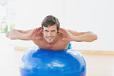 Smiling shirtless man exercising on fitness ball in gym