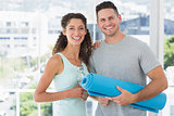 Happy couple holding water bottle and exercise mat at gym