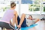 Trainer assisting fit man in doing sits