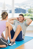 Trainer assisting fit man in doing sits up