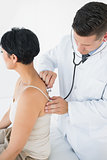 Doctor using stethoscope on back of woman