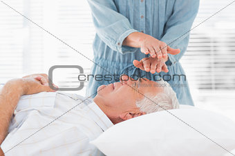 Massage therapist performing Reiki over man