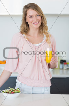 Woman with salad holding orange juice in kitchen
