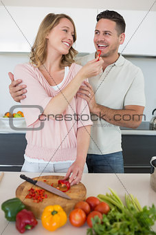 Woman feeding capsicum to man in kitchen
