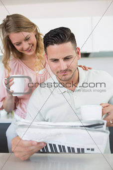 Couple reading newspaper while holding coffee mugs