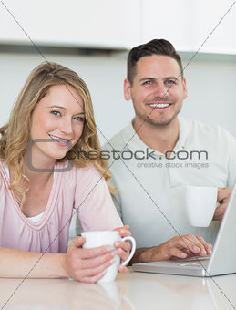 Couple with coffee mugs and laptop sitting at table